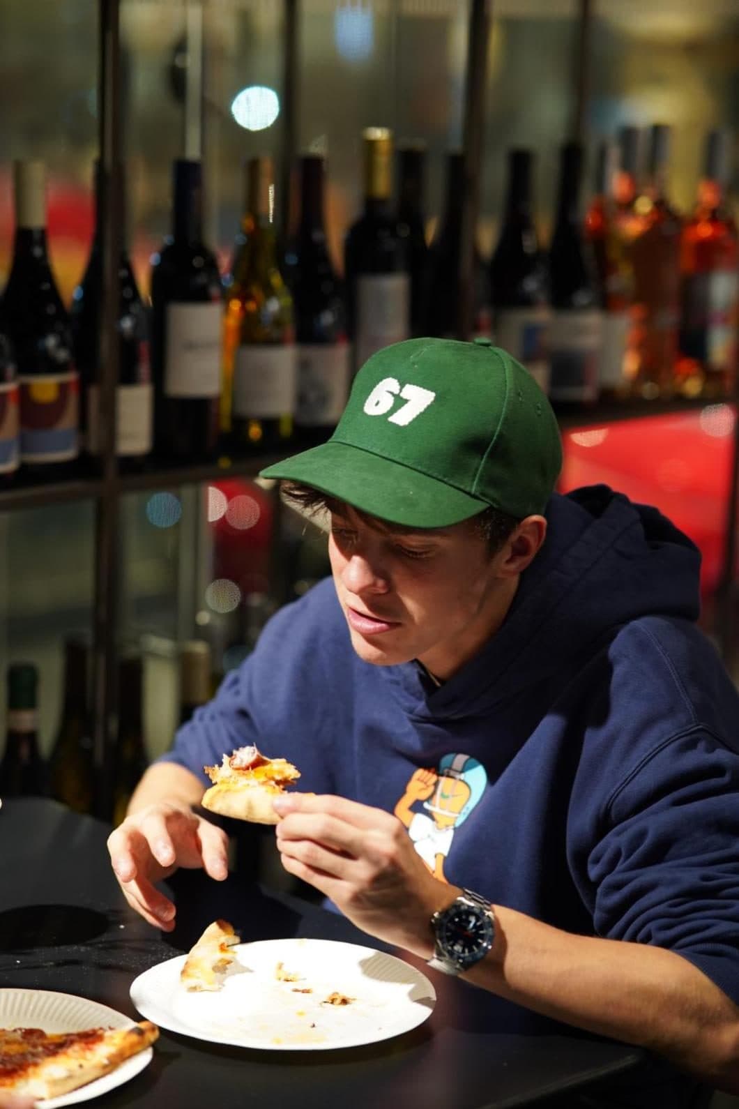 A guest in a 67 cap eating a slice at the bar