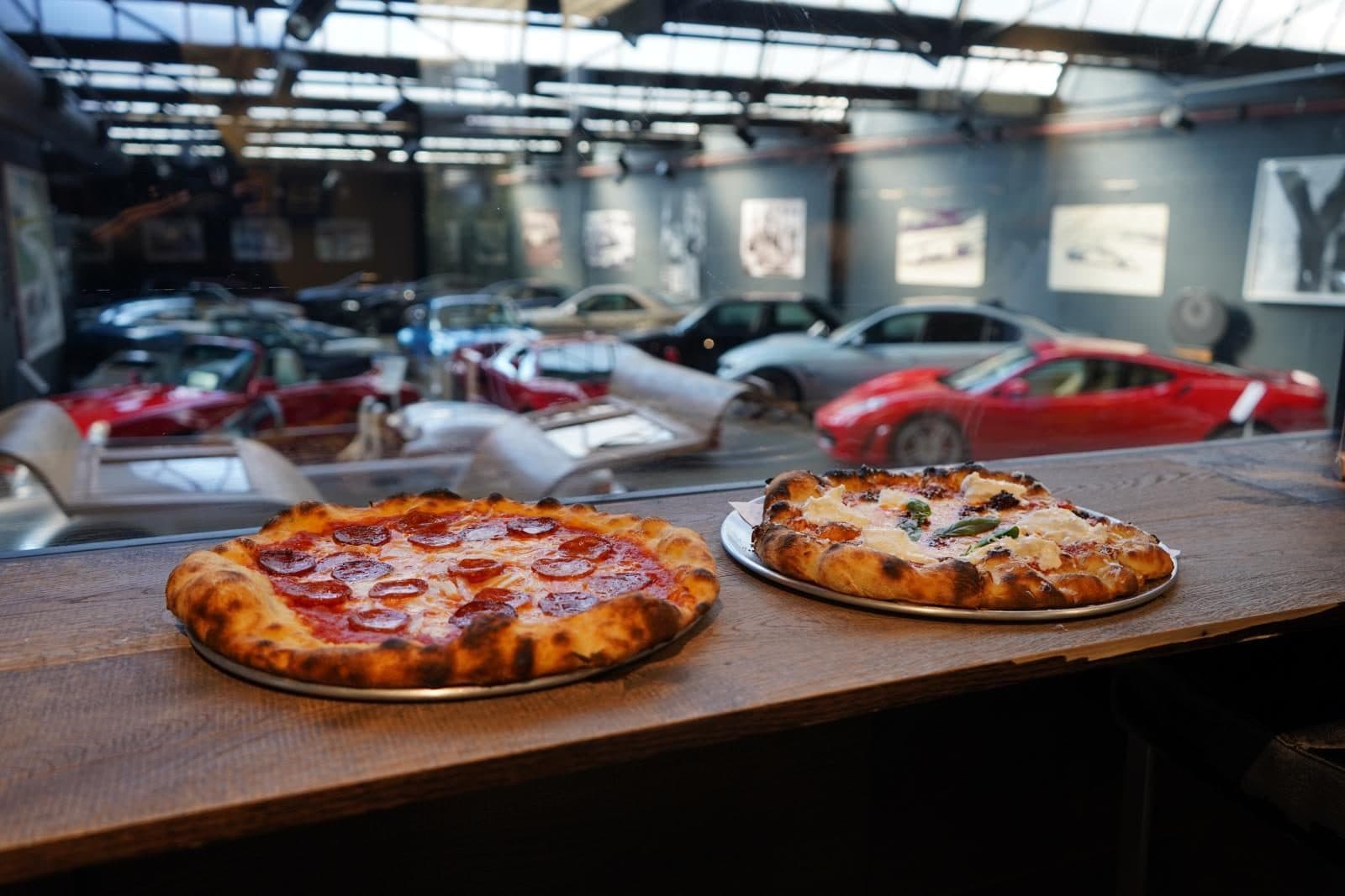 Two pizzas on the counter with classic cars behind