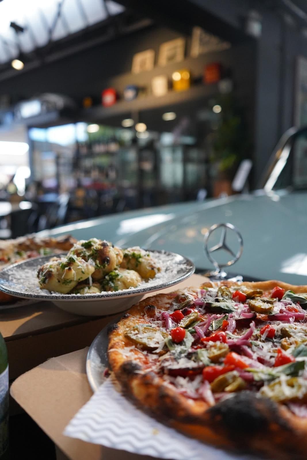 A pizza and a plate of garlic knots on a table beside a classic Mercedes